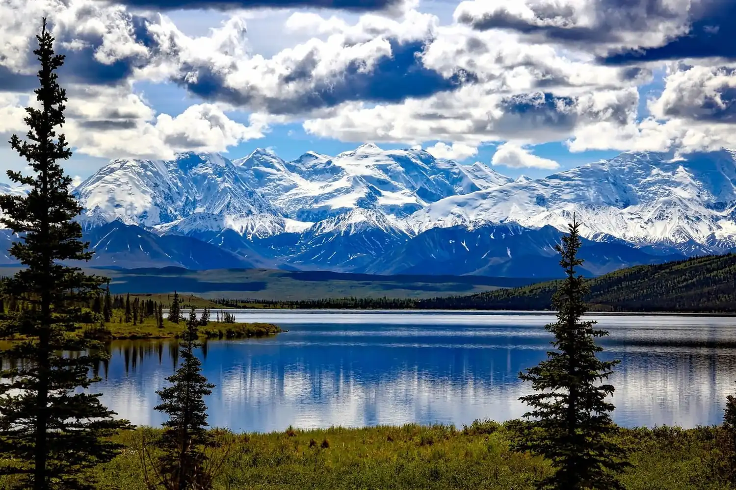 Alaskan mountain range reflected in a still lake under cloud-dappled sky